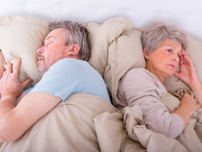 Älteres Ehepaar liegt im Bett. Er schnarcht und sie kann nicht schlafen.