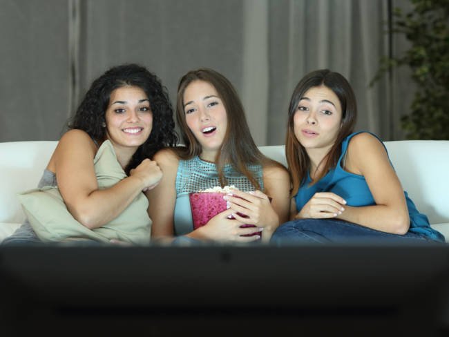 Drei junge Mädchen schauen zu dritt eine Fernsehsendung