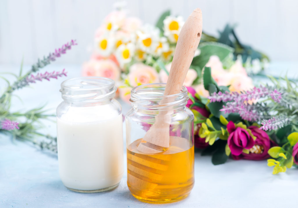 Milch und Honig stehen in Gläsern auf dem Tisch, im Hintergrund liegen Blumen